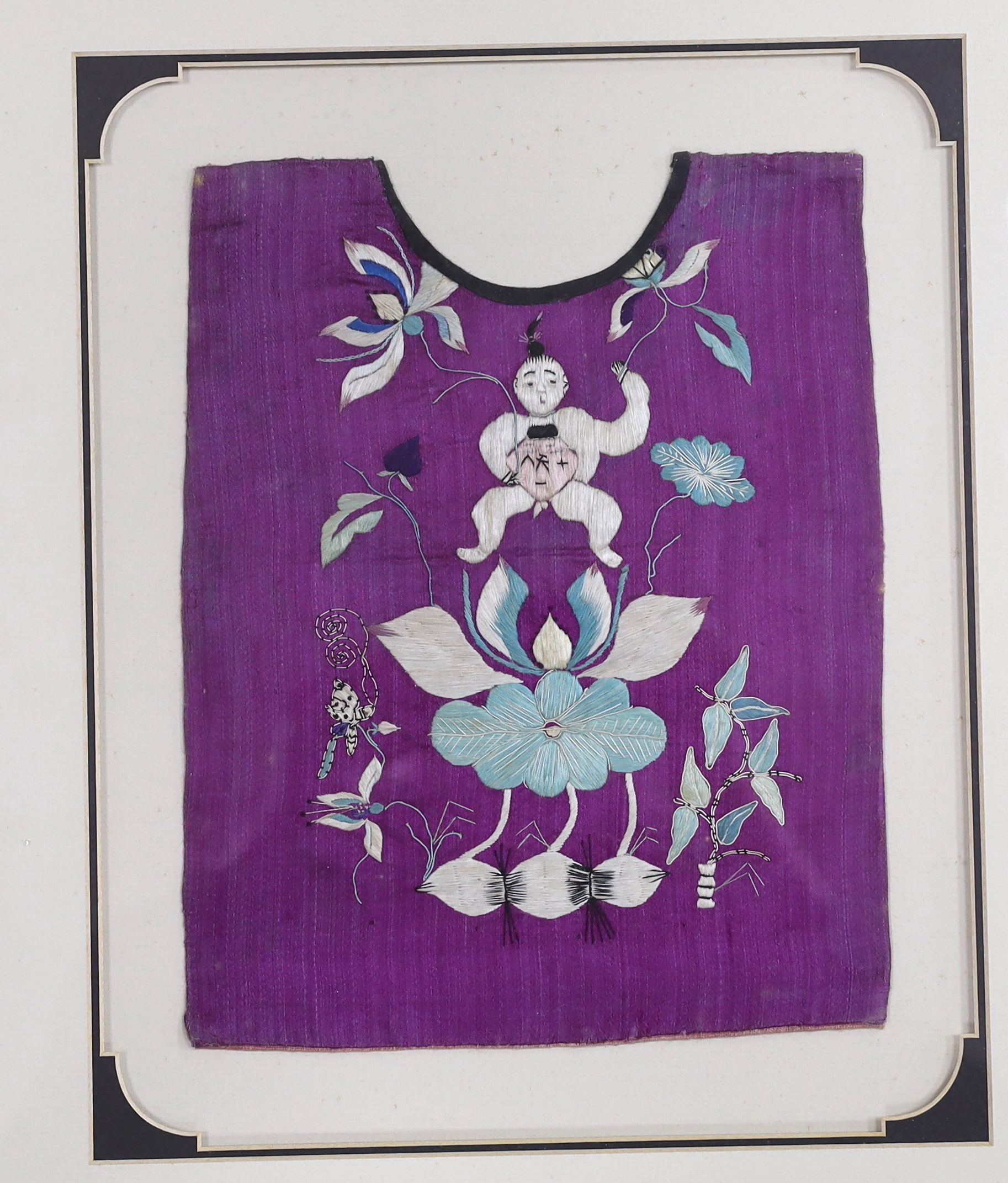 Three early 20th century Chinese framed embroideries: two purple baby’s bibs embroidered with multi-coloured silk threads, and another red silk child’s “romper suit”, embroidered with white and pastel embroidery, mounted